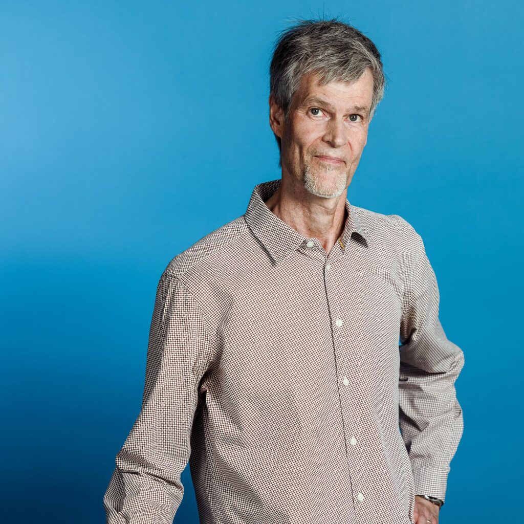 Torso-Ansicht eines grauhaarigen schlanken Mannes in gemustertem Hemd vor marineblauem Fond