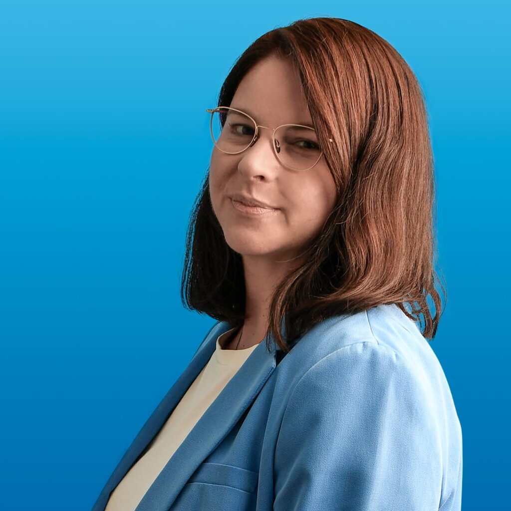 Torso-Ansicht einer dunkelhaarigen Dame in himmelblauem Jackett vor marineblauem Fond