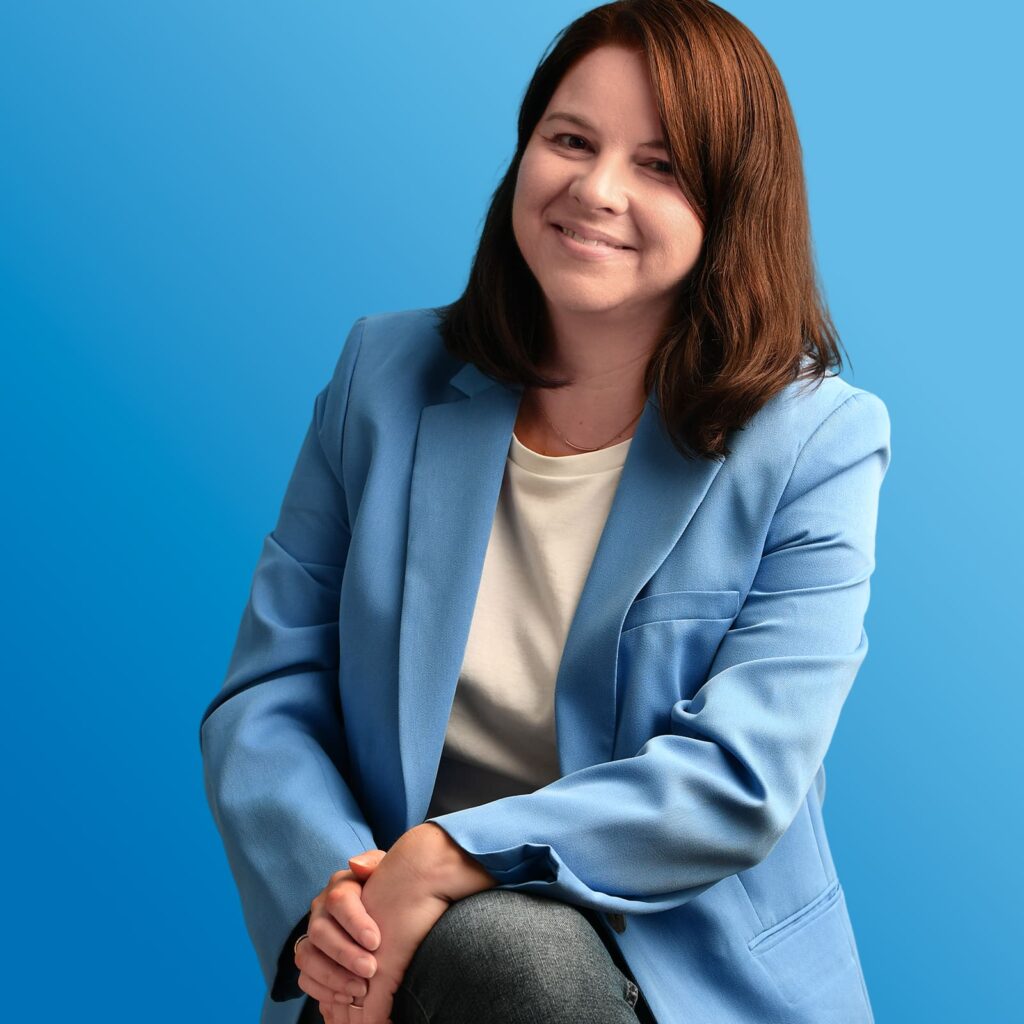 Torso-Ansicht einer dunkelhaarigen Dame in himmelblauem Jackett vor marineblauem Fond